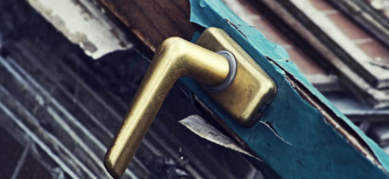 Türgriff aus Messing an altem Türrahmen mit splitternder Farblackierung und verwittertem Holz zur Entrümpelung in Hamburg-Nord